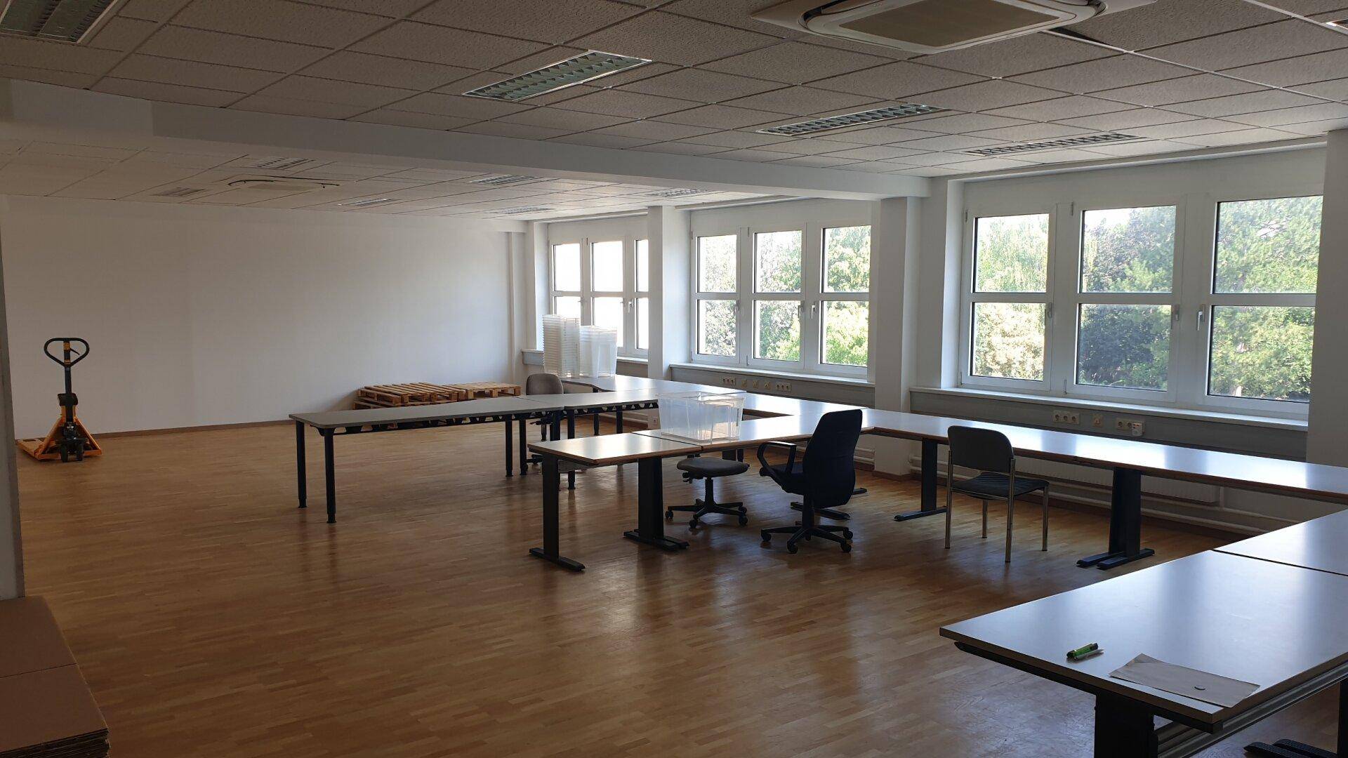 Großer, heller Konferenzraum mit Holzboden, vielen Fenstern und flexibler Möblierung für Veranstaltungen.