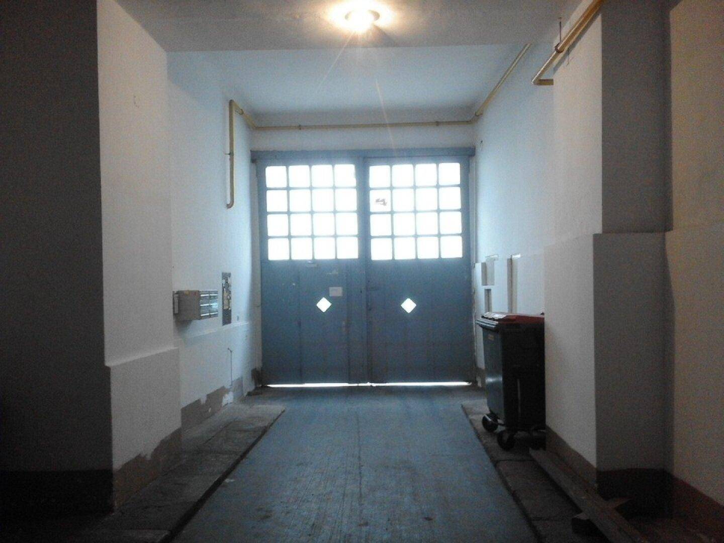 Geräumiger Garagenzugang mit hohen Decken, Betonboden und großen Fenstertüren, die Tageslicht hereinlassen.