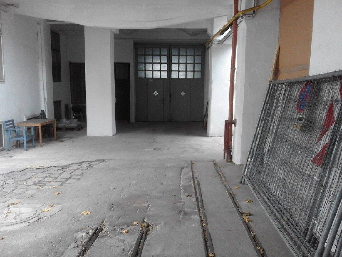 Großer Außenbereich oder Hof mit Betonboden, Säulen und den gleichen Doppeltüren wie im Innenbereich.
