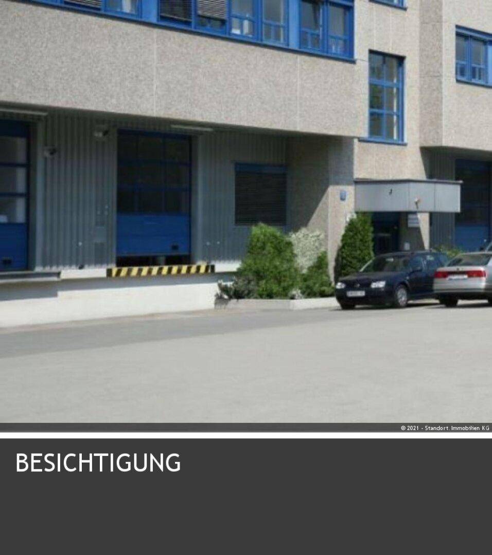Außenansicht eines Industriegebäudes mit Laderampen und geparkten Autos vor dem Eingangsbereich.