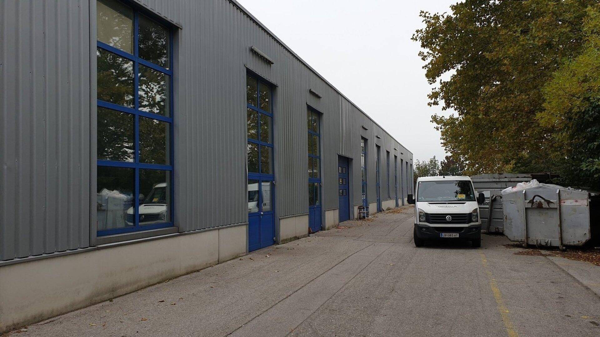 Langes Industriegebäude mit großen Fenstern, blauen Türen und einem geparkten Lieferwagen davor.