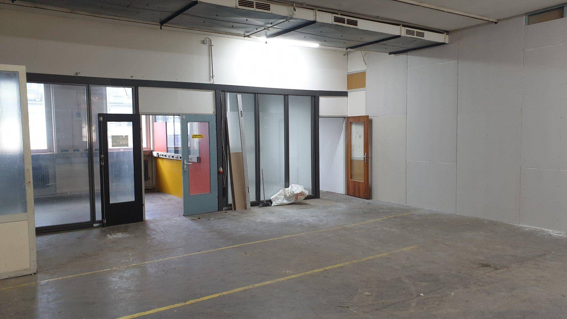 Geräumiger Industrieraum mit Betonboden, Trennwänden und Glastüren, ideal für verschiedene gewerbliche Zwecke.