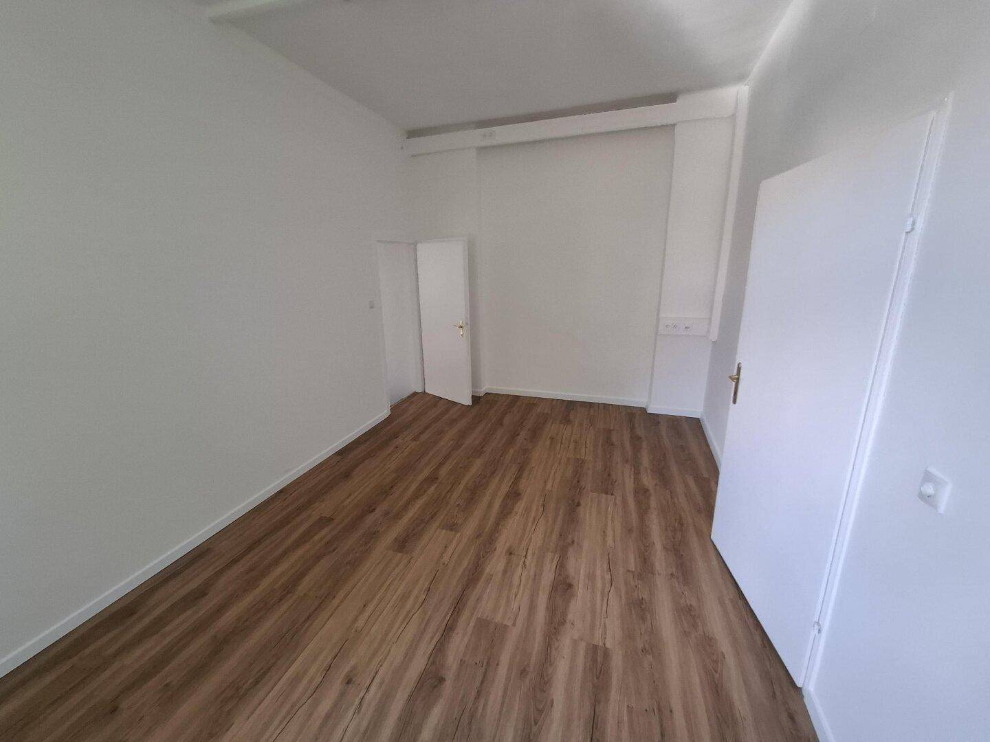 Heller, leerer Raum mit Laminatboden und weißen Wänden, bereit für die individuelle Gestaltung.