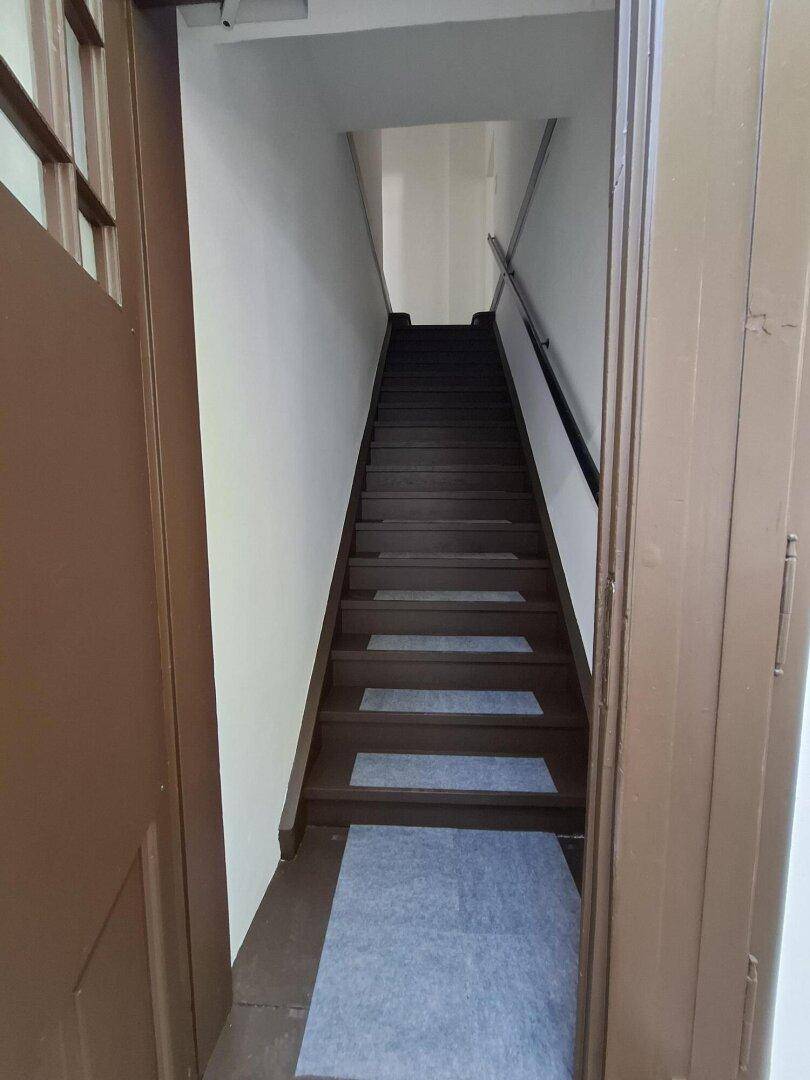 Treppenhaus mit dunklen Holzstufen und hellen Teppichläufern, die nach oben führen.