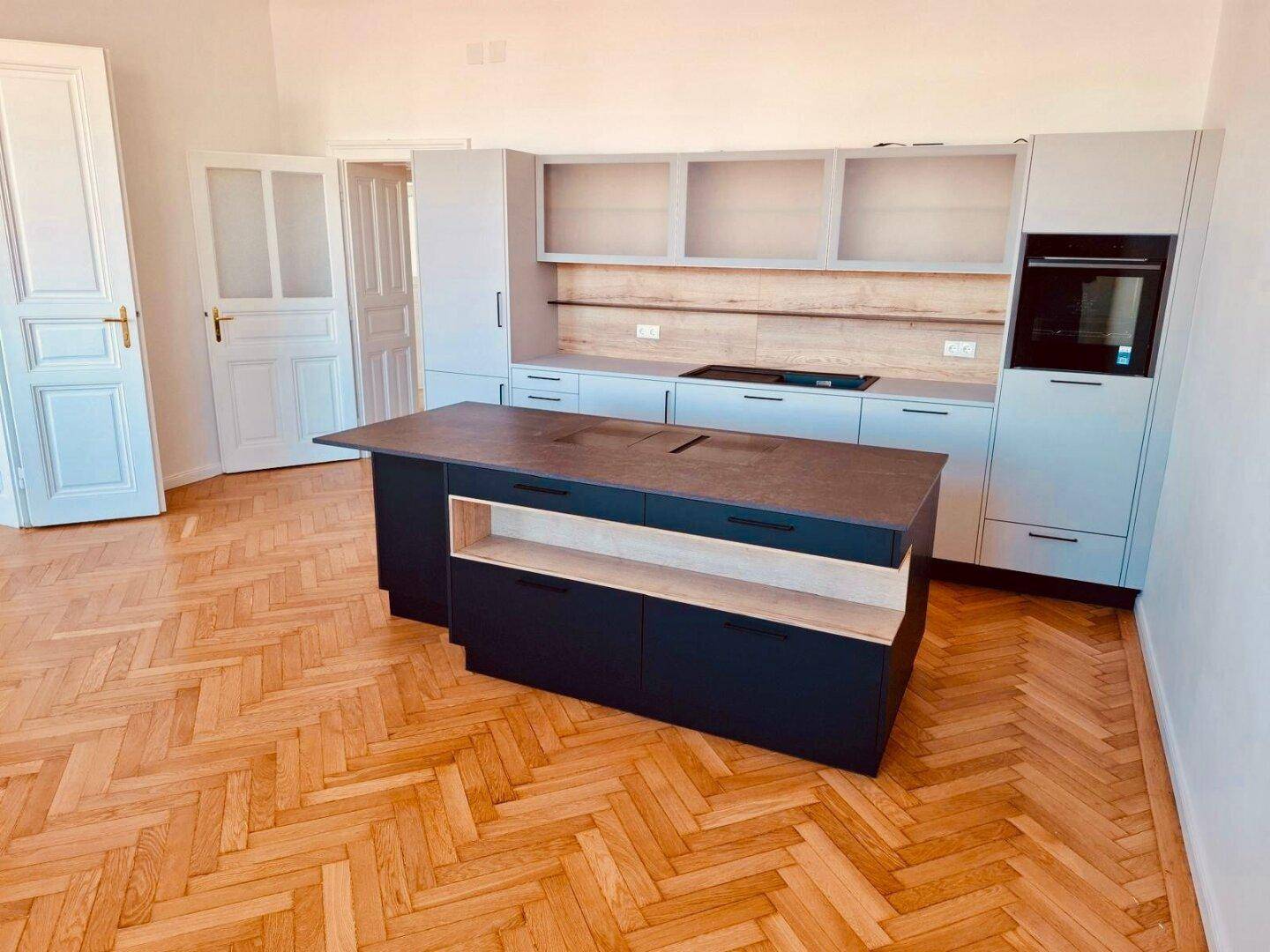 Geräumige Küche mit moderner Kücheninsel, Einbaugeräten und hellem Fischgrätparkettboden.