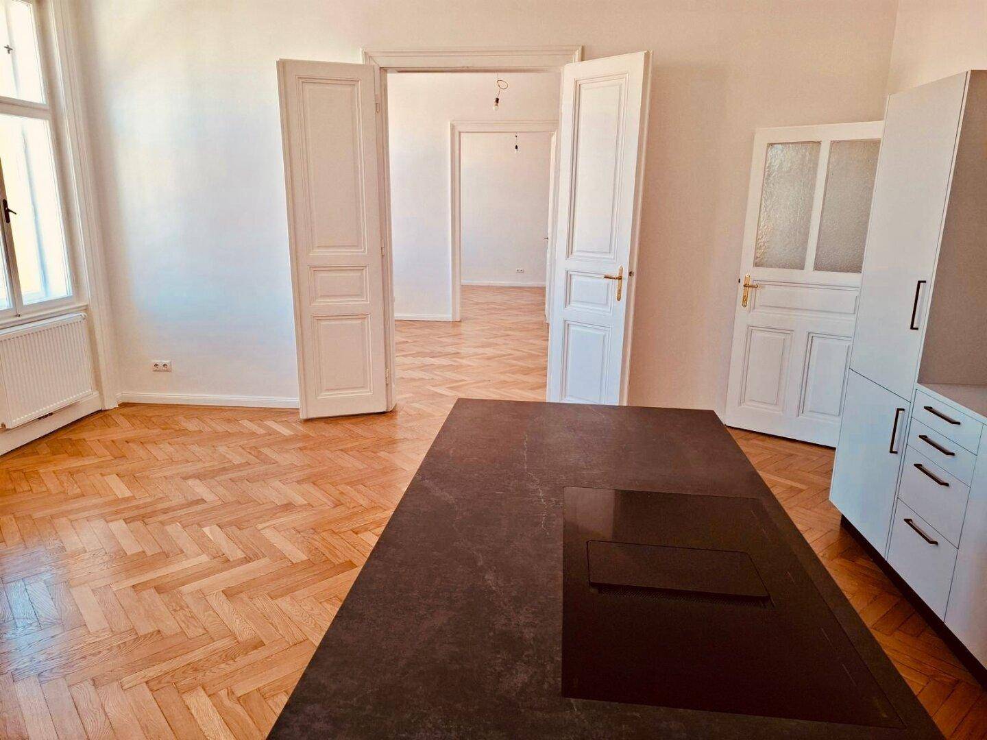 Moderne Küche mit dunkler Arbeitsplatte und integriertem Kochfeld, verbunden mit weiteren Räumen.