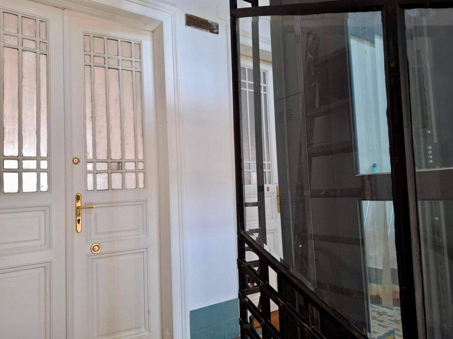 Heller Eingangsbereich mit klassischer Tür und modernem Aufzug im Treppenhaus des Altbaus.