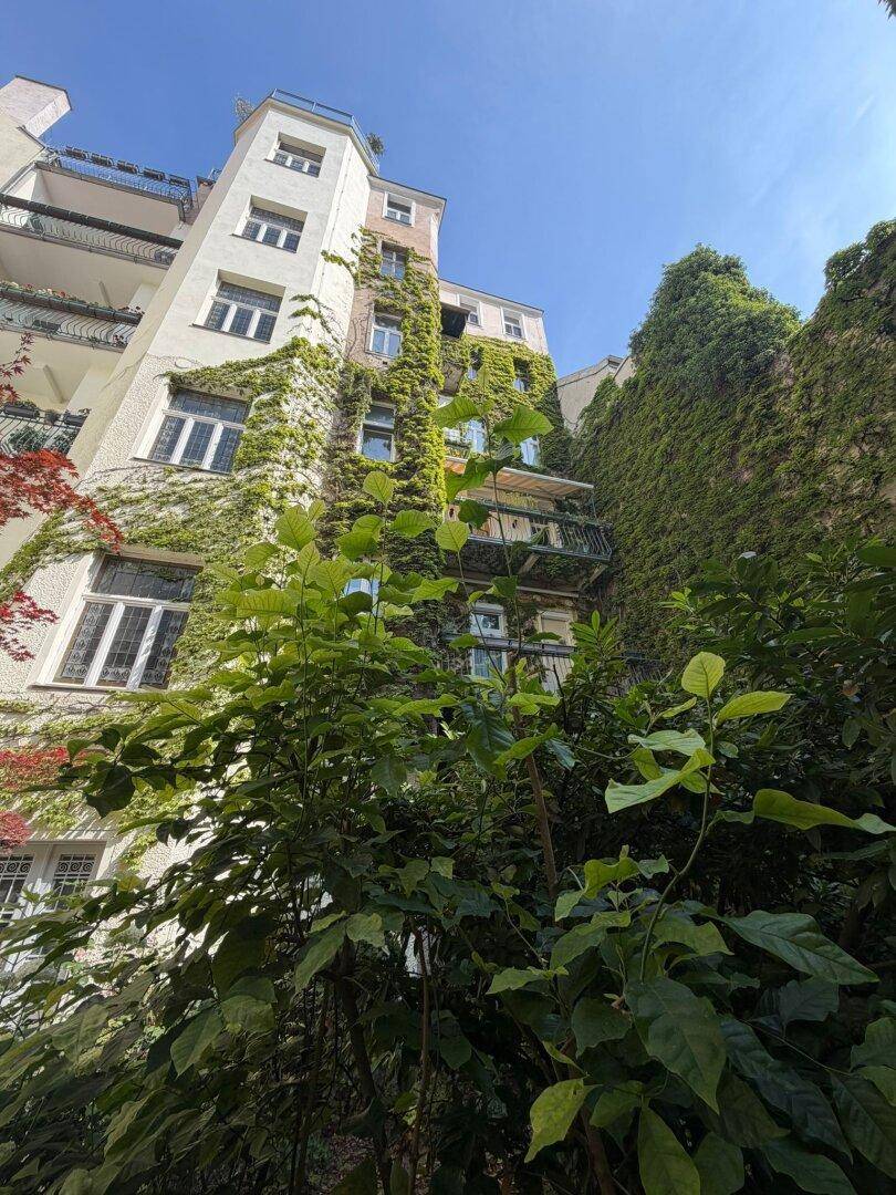 Grüne Fassade eines Gebäudes, üppig bewachsen mit Efeu und Balkonen.