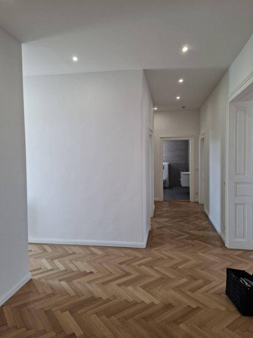 Langer Flur mit hochwertigem Fischgrätparkett und Deckenstrahlern, mit Blick in ein Badezimmer.