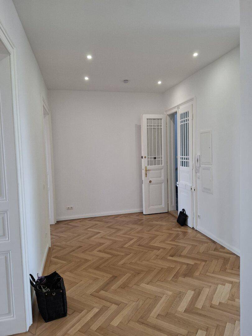 Heller Flur mit elegantem Fischgrätparkett und modernen Einbaustrahlern, der zu weiteren Räumen führt.
