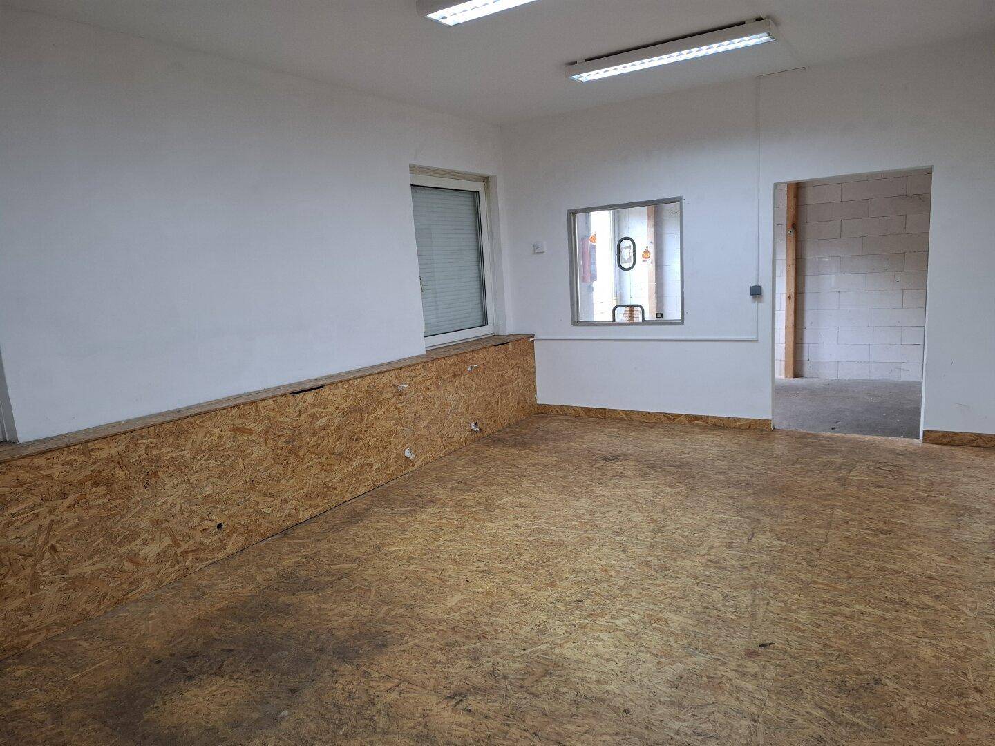 Kleiner Raum mit weißen Wänden, OSB-Plattenverkleidung und einem Fenster mit Rollladen.