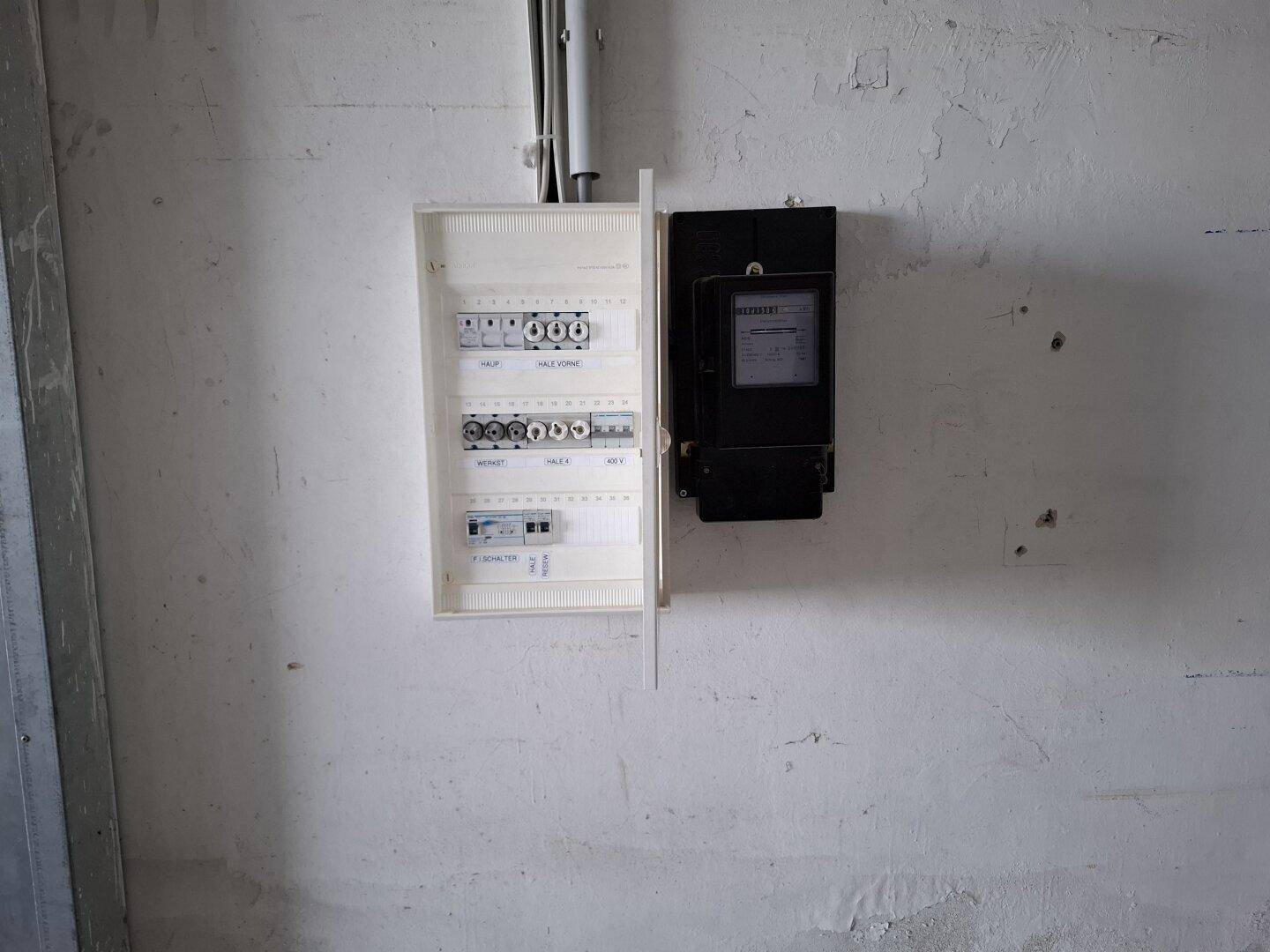 Nahaufnahme eines elektrischen Schaltkastens und eines Stromzählers an einer weißen Wand.