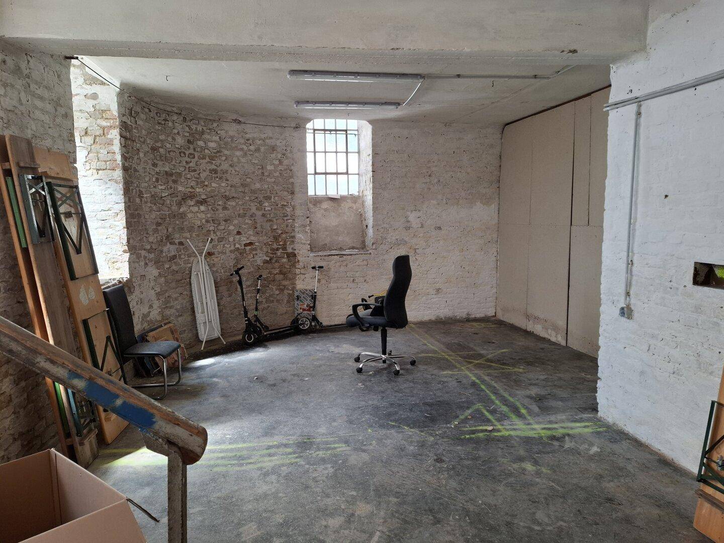 Großer, unfertiger Raum mit unverputzten Ziegelwänden, Betonboden und einem vergitterten Fenster, ideal für Renovierung.