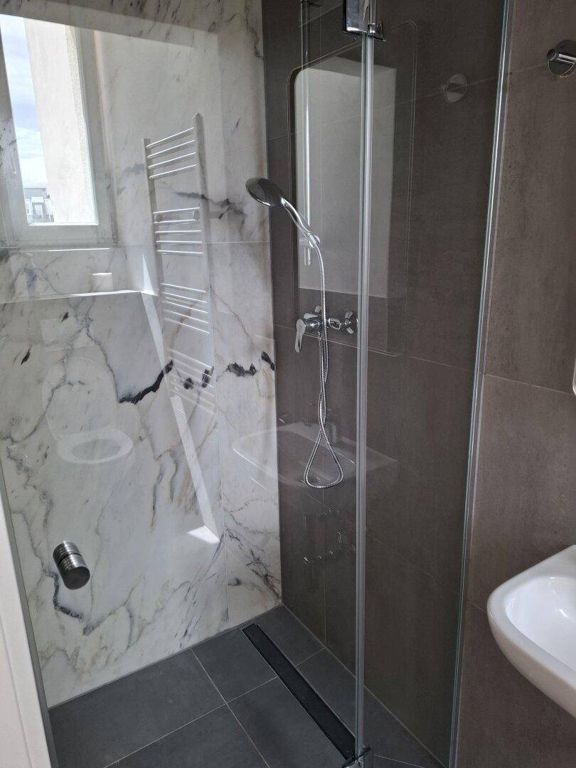 Modernes Badezimmer mit begehbarer Dusche, Marmoroptik-Fliesen und Fenster für natürliches Licht.