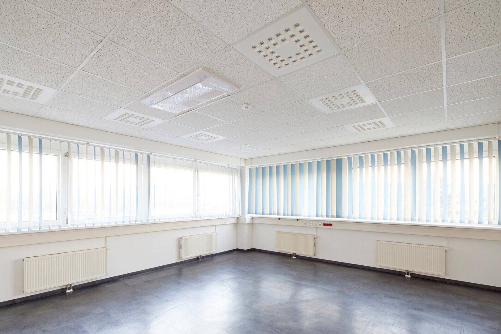 Geräumiges Büro mit vielen Fenstern, vertikalen Jalousien und dunklem Betonboden.