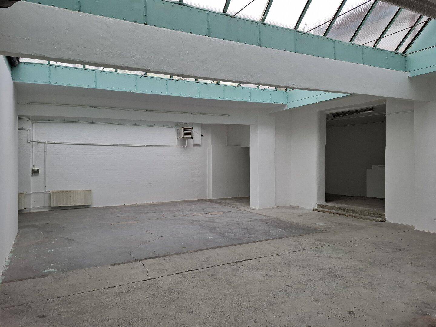 Heller Industrieraum mit Betonboden und großem Glasdach, bietet viel Platz und natürliches Licht.