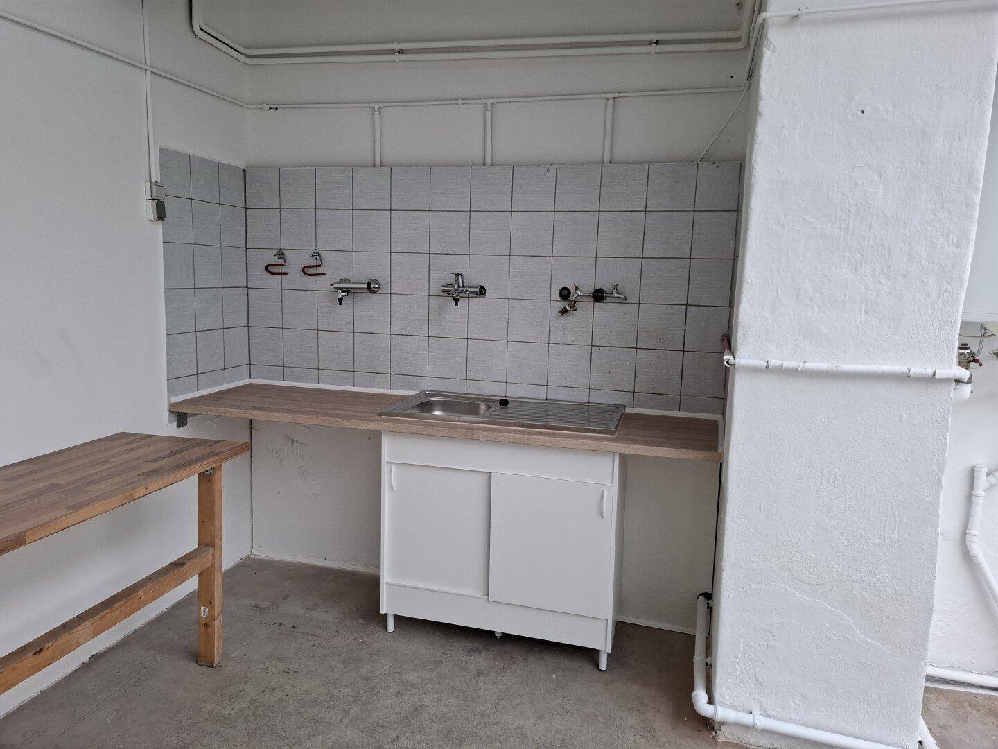 Einfacher Küchenbereich mit Spülbecken, gefliestem Spritzschutz und Holzwerkbank in einem funktionalen Raum.