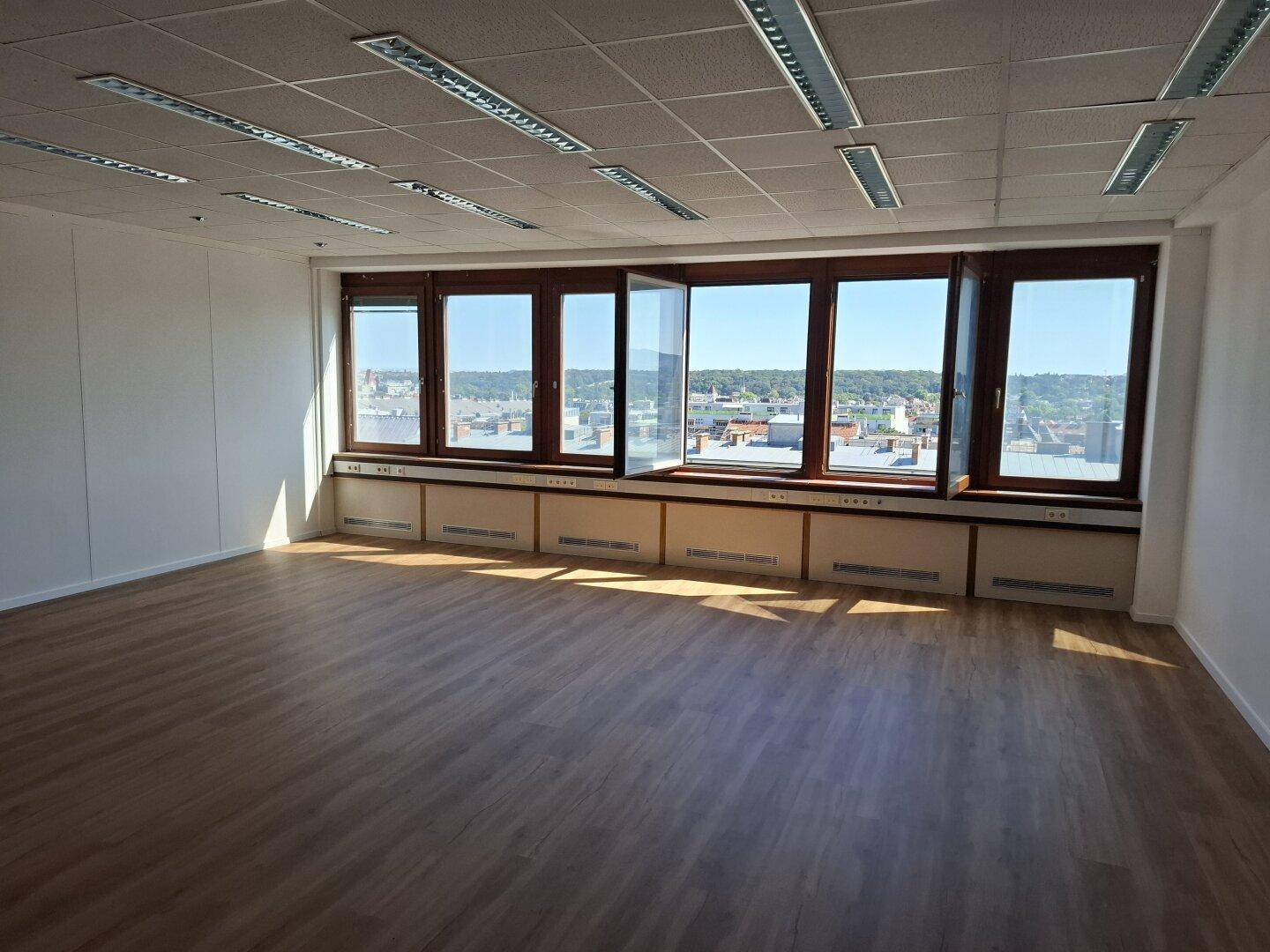 Großer, heller Büroraum mit vielen Fenstern, die einen Panoramablick auf die Stadt ermöglichen.