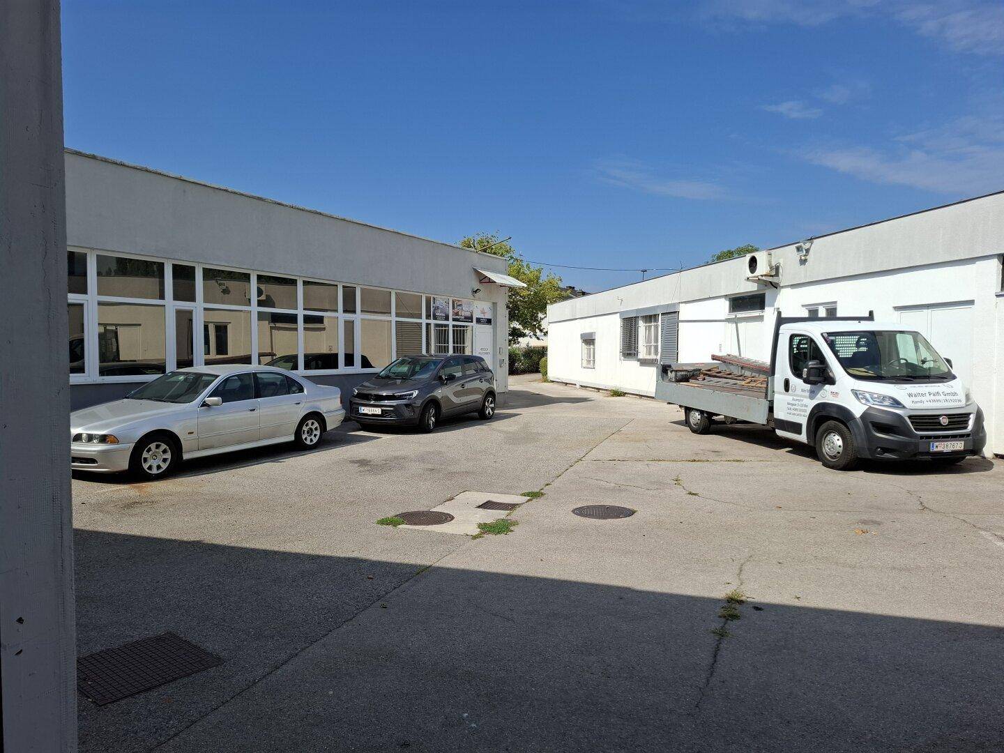 Außenansicht des Gebäudes mit mehreren geparkten Fahrzeugen und einem Lieferwagen auf dem Vorplatz.