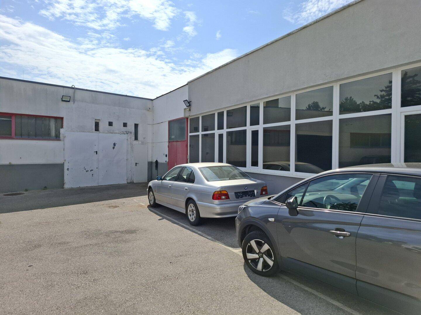Seitenansicht des Gebäudes mit großen Fenstern und geparkten Autos auf dem asphaltierten Parkplatz.