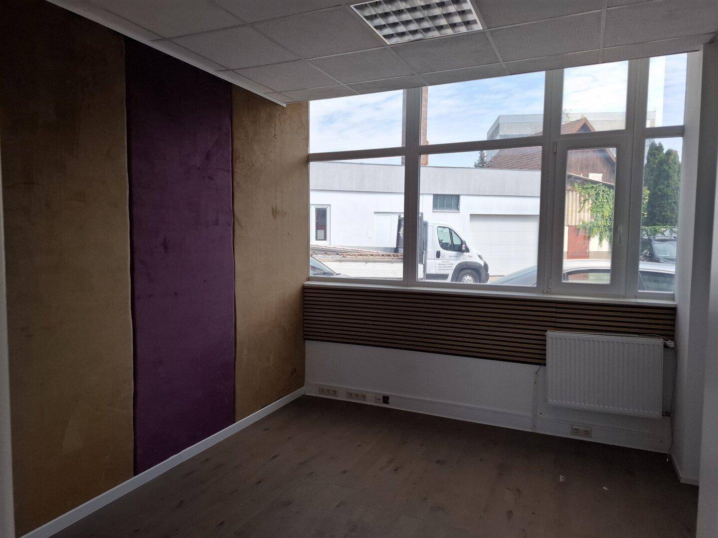 Büro mit Holzboden, großen Fenstern und einer Wand mit lila und braunen Akzenten.