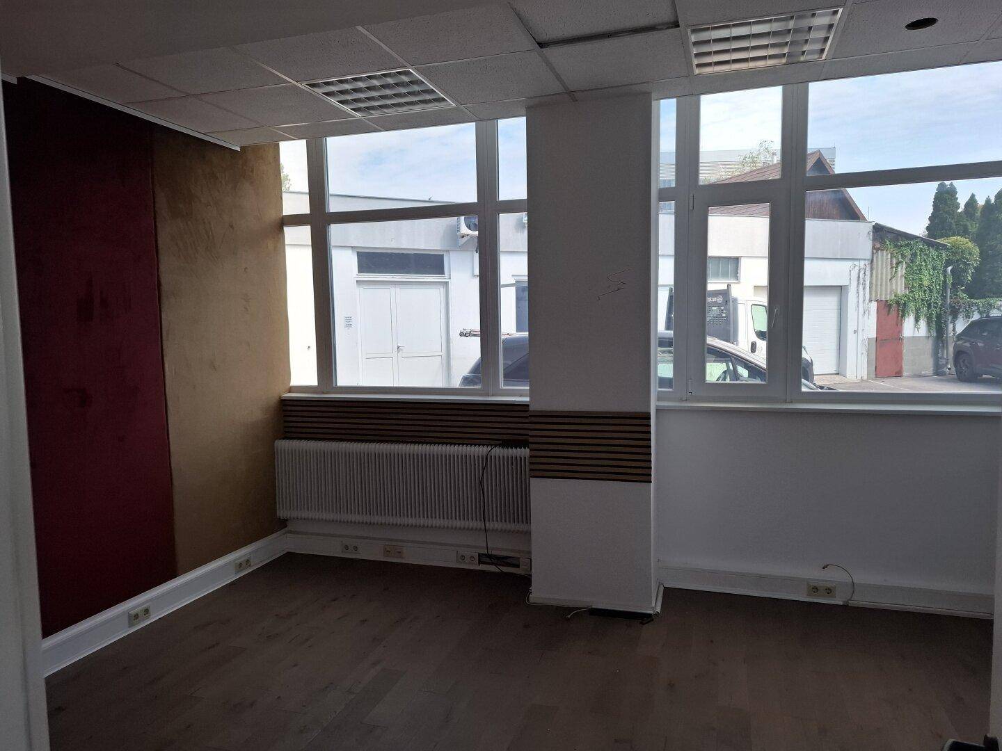 Büro mit Holzboden, großen Fenstern und einer Säule in der Mitte des Raumes.
