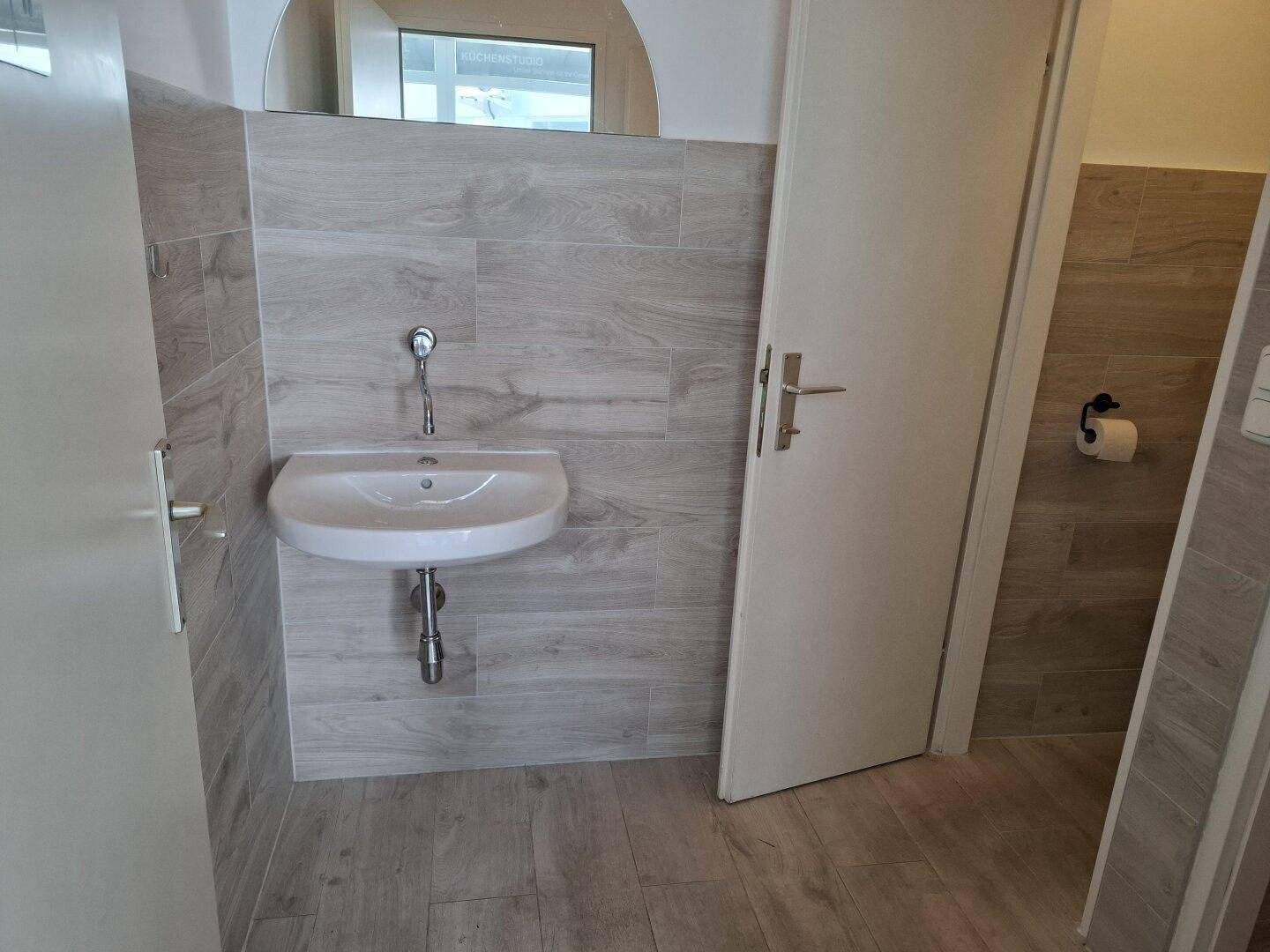 Waschraum mit modernem Waschbecken, Spiegel und holzgemusterten Fliesen an den Wänden.