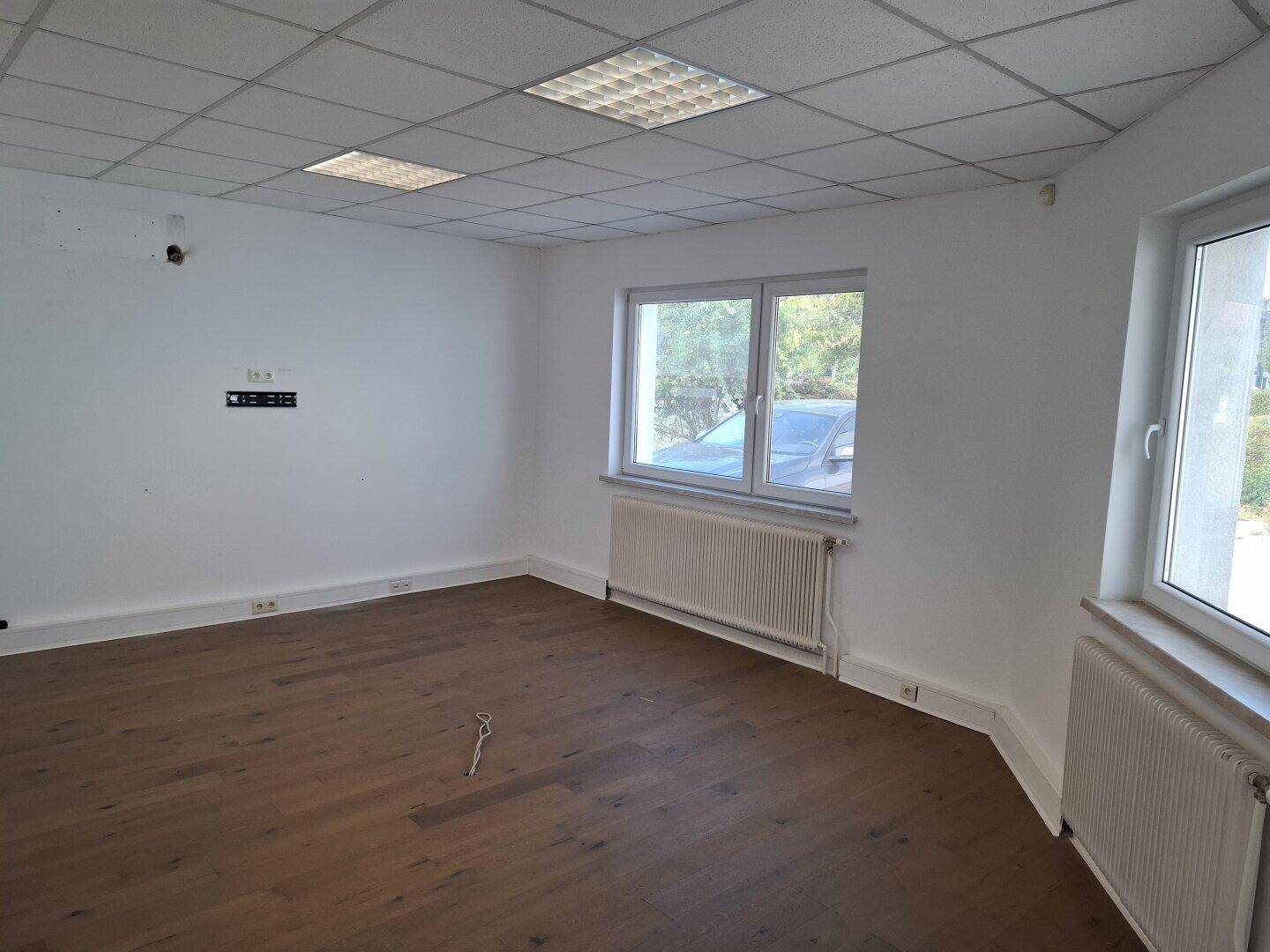 Helles Büro mit Holzboden, weißen Wänden und großen Fenstern, die viel Tageslicht hereinlassen.