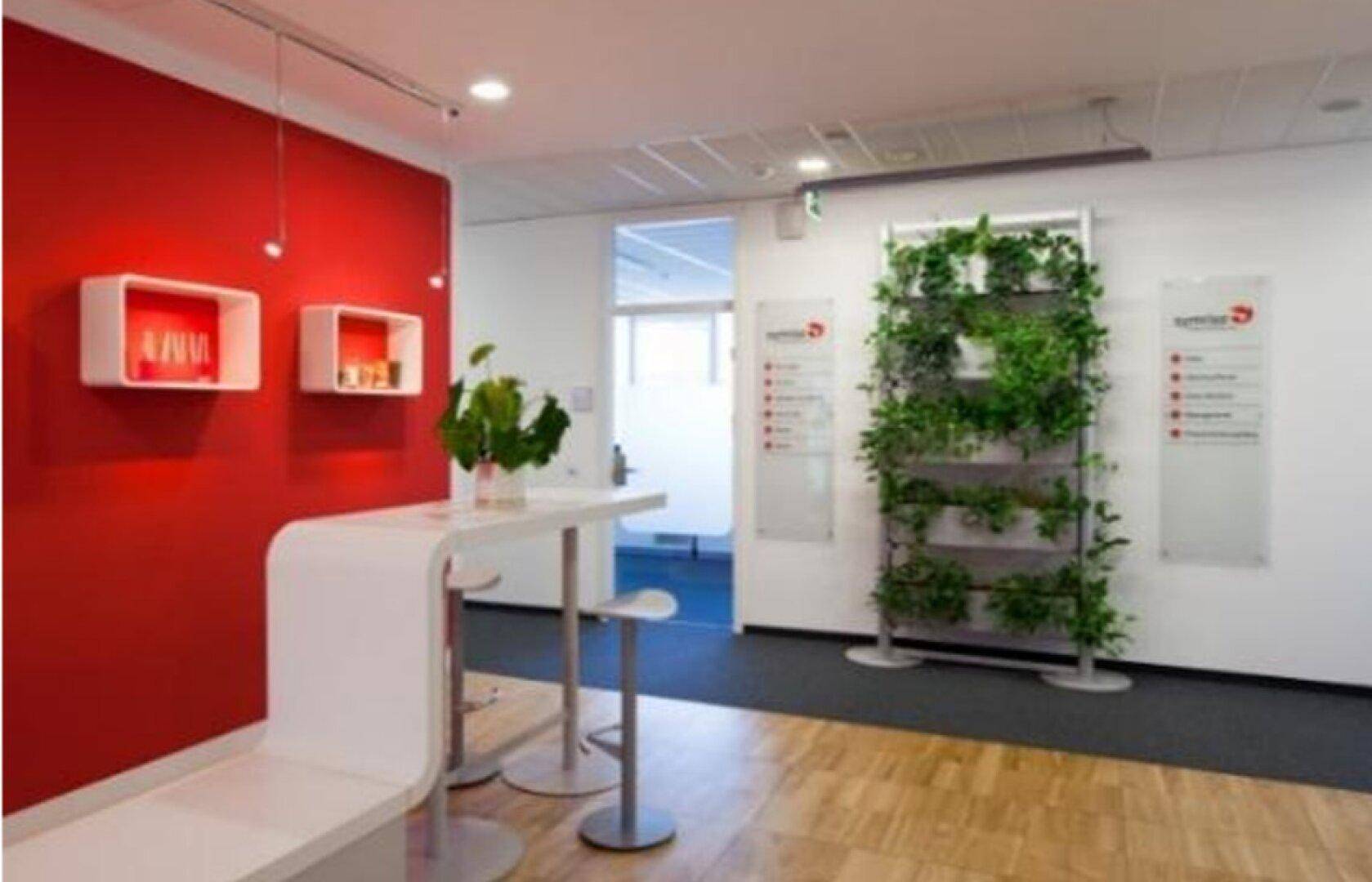 Empfangsbereich mit roter Akzentwand, Stehtisch und einer vertikalen Pflanzenwand als Dekoration.