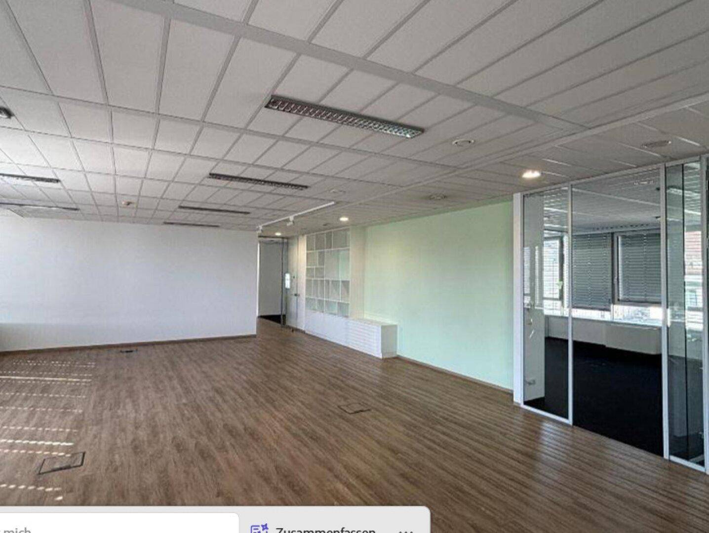 Geräumiger Büroraum mit Holzboden, hellgrüner Wand und Glasabtrennungen für flexible Arbeitsbereiche.