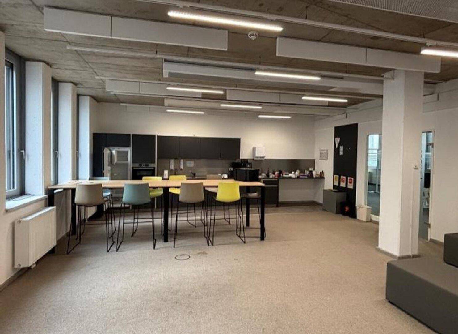 Große Büroküche mit langer Theke, modernen Geräten und Essbereich für Mitarbeiter.