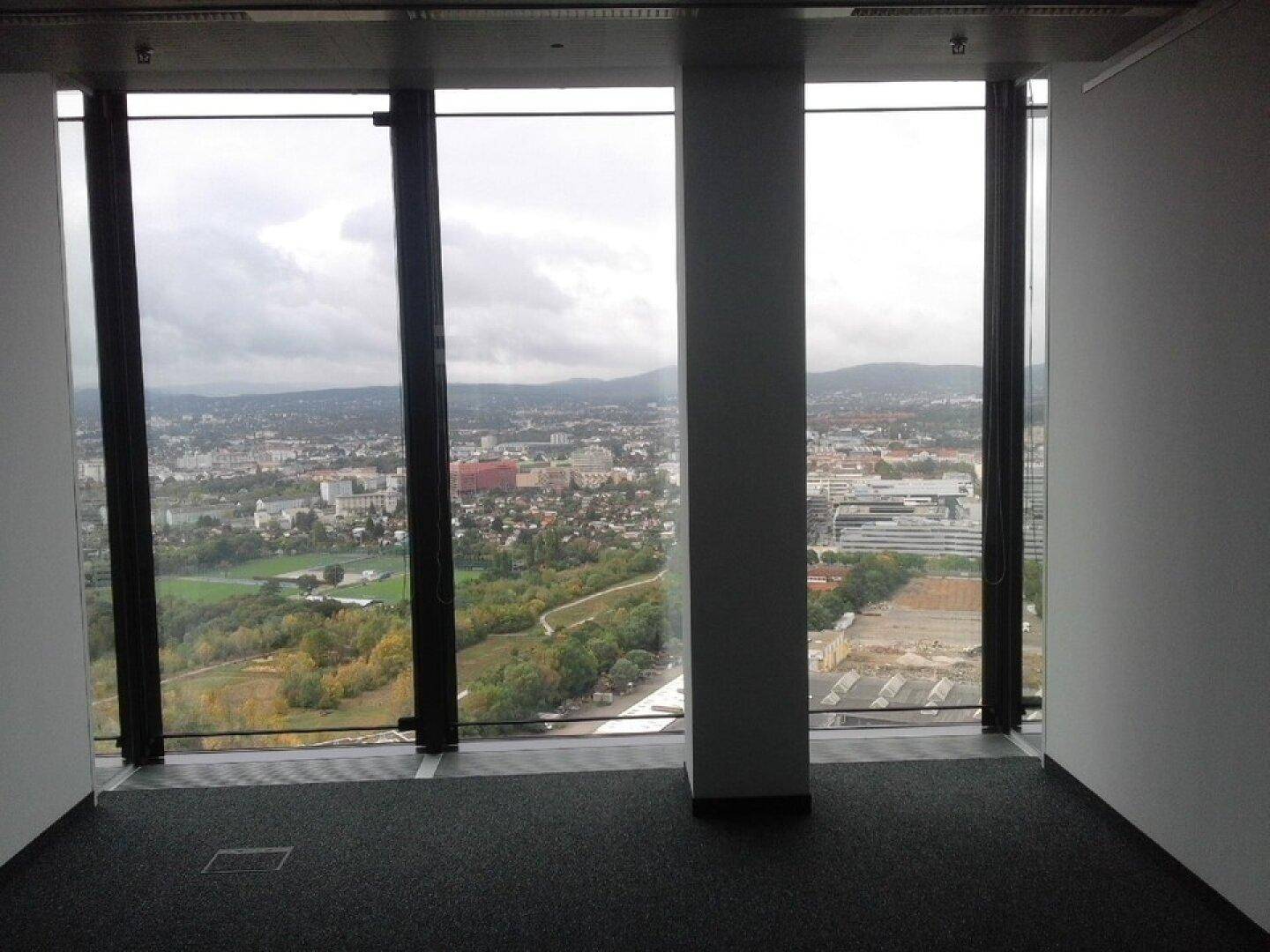 Geräumiger Büroraum mit großen Fenstern und weitem Blick über die Stadt und grüne Flächen.