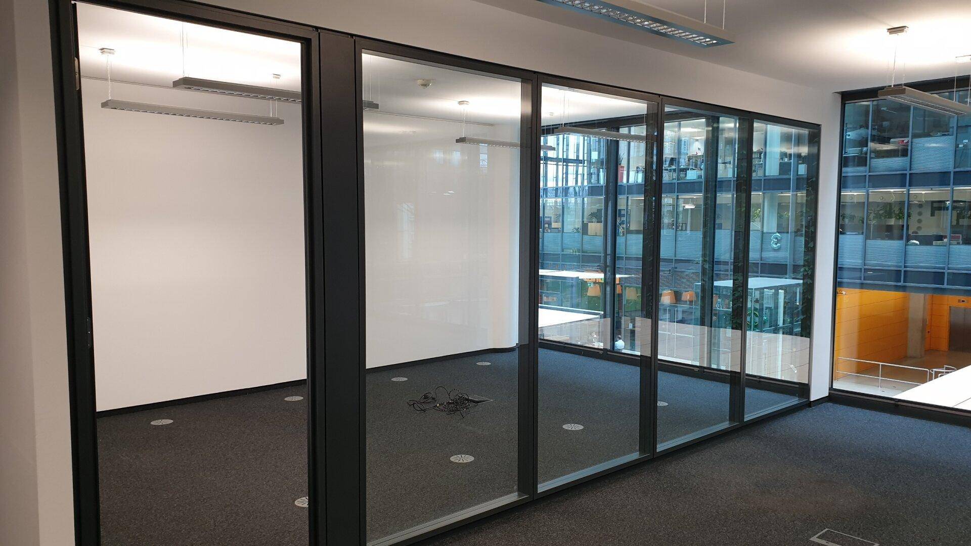 Büroinnenraum mit Glaswänden, die einen separaten Bereich abtrennen, und Blick auf umliegende Gebäude.