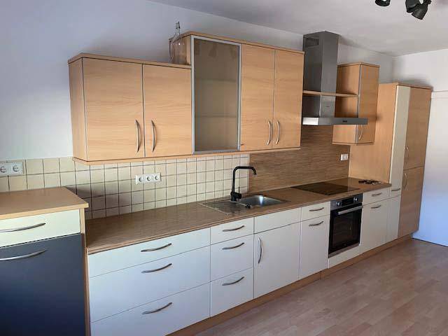 Moderne Einbauküche mit hellen Holz- und weißen Fronten, Spüle und Kochfeld.