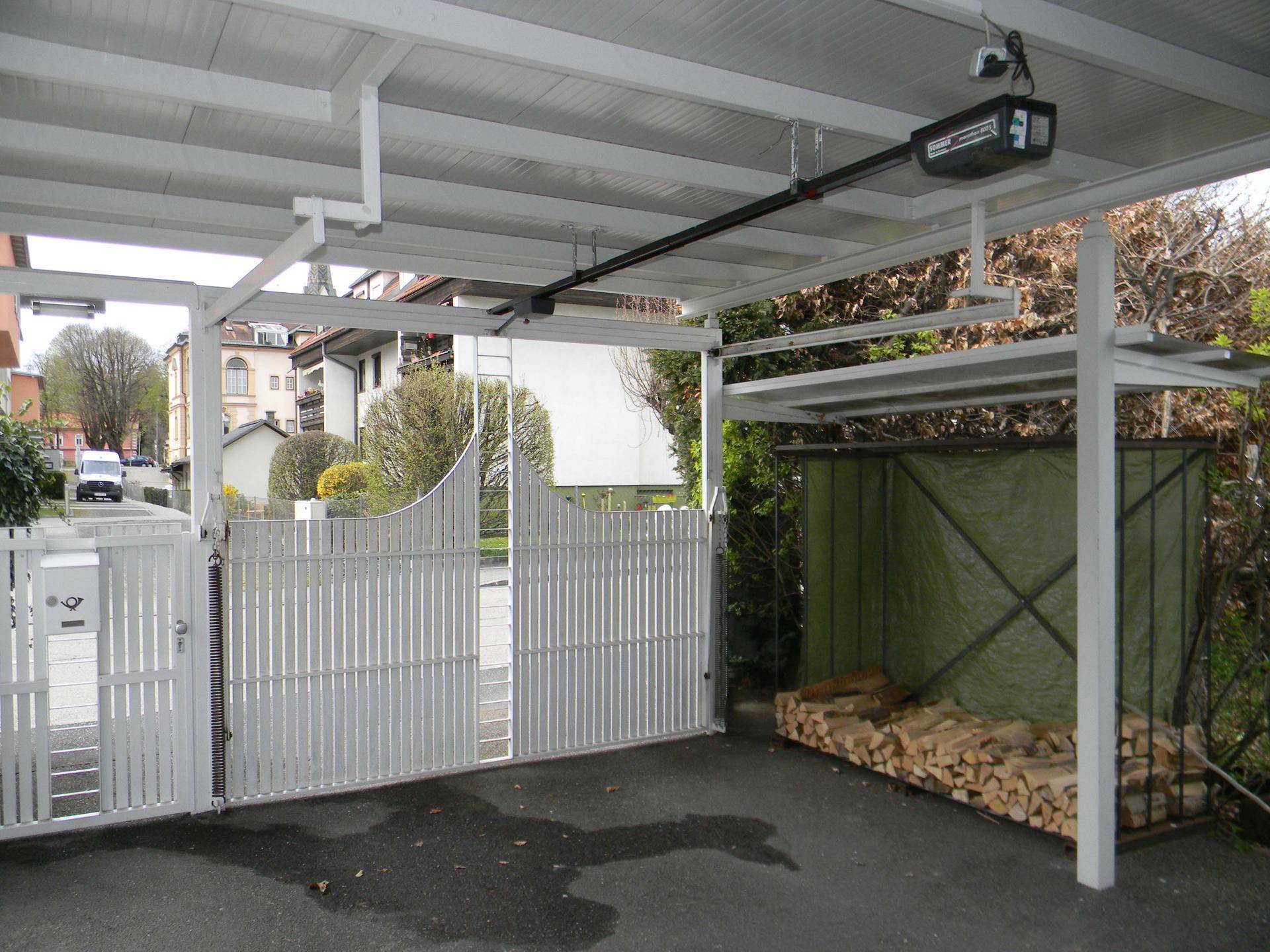 Überdachter Carport mit automatischem Tor und Lagerplatz für Brennholz im Außenbereich.