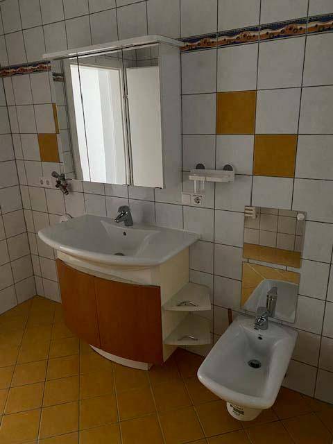 Badezimmer mit Waschtisch, Spiegelschrank, Bidet und gelben Bodenfliesen.