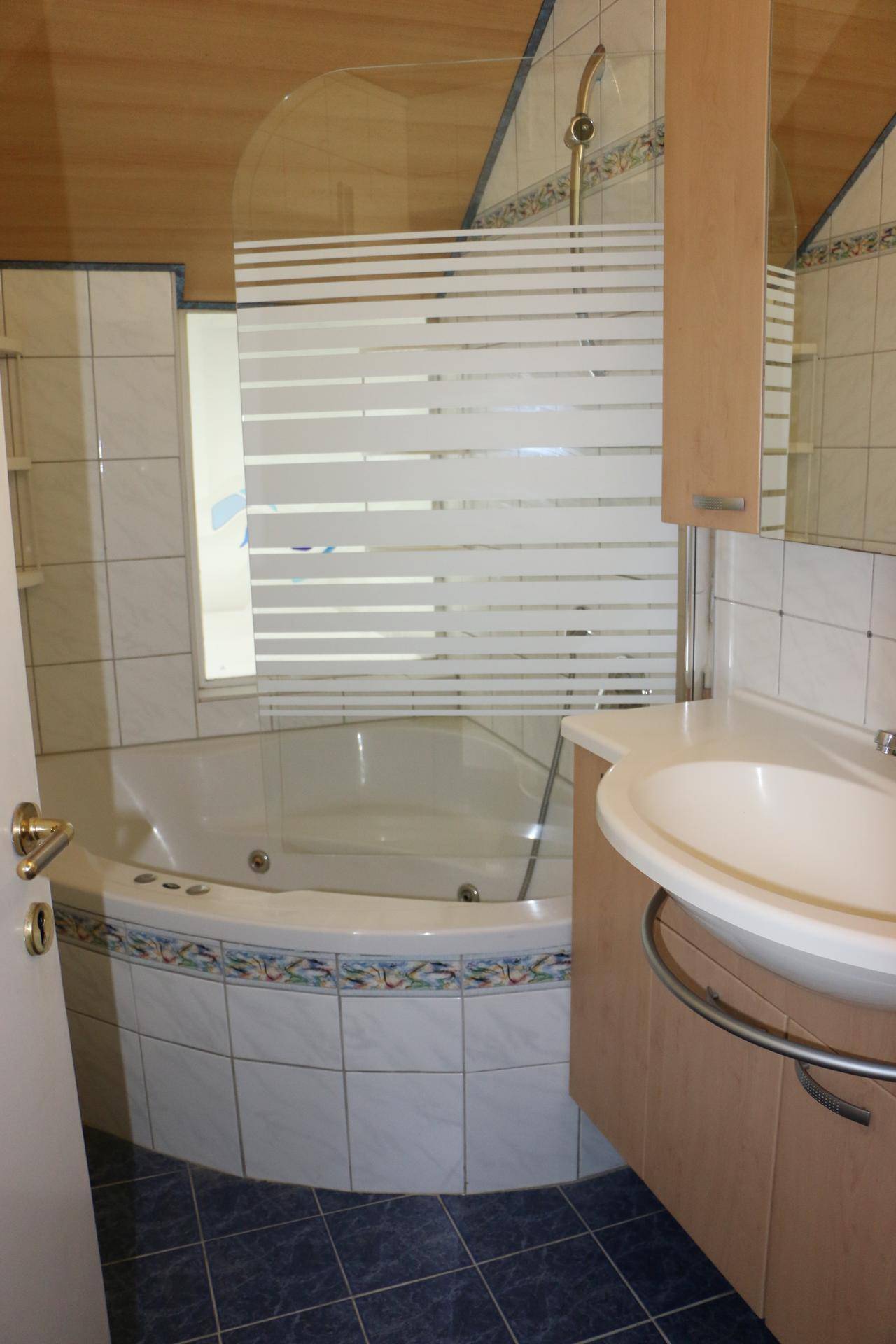 Badezimmer mit Eckbadewanne, Waschbecken und blauen Bodenfliesen.