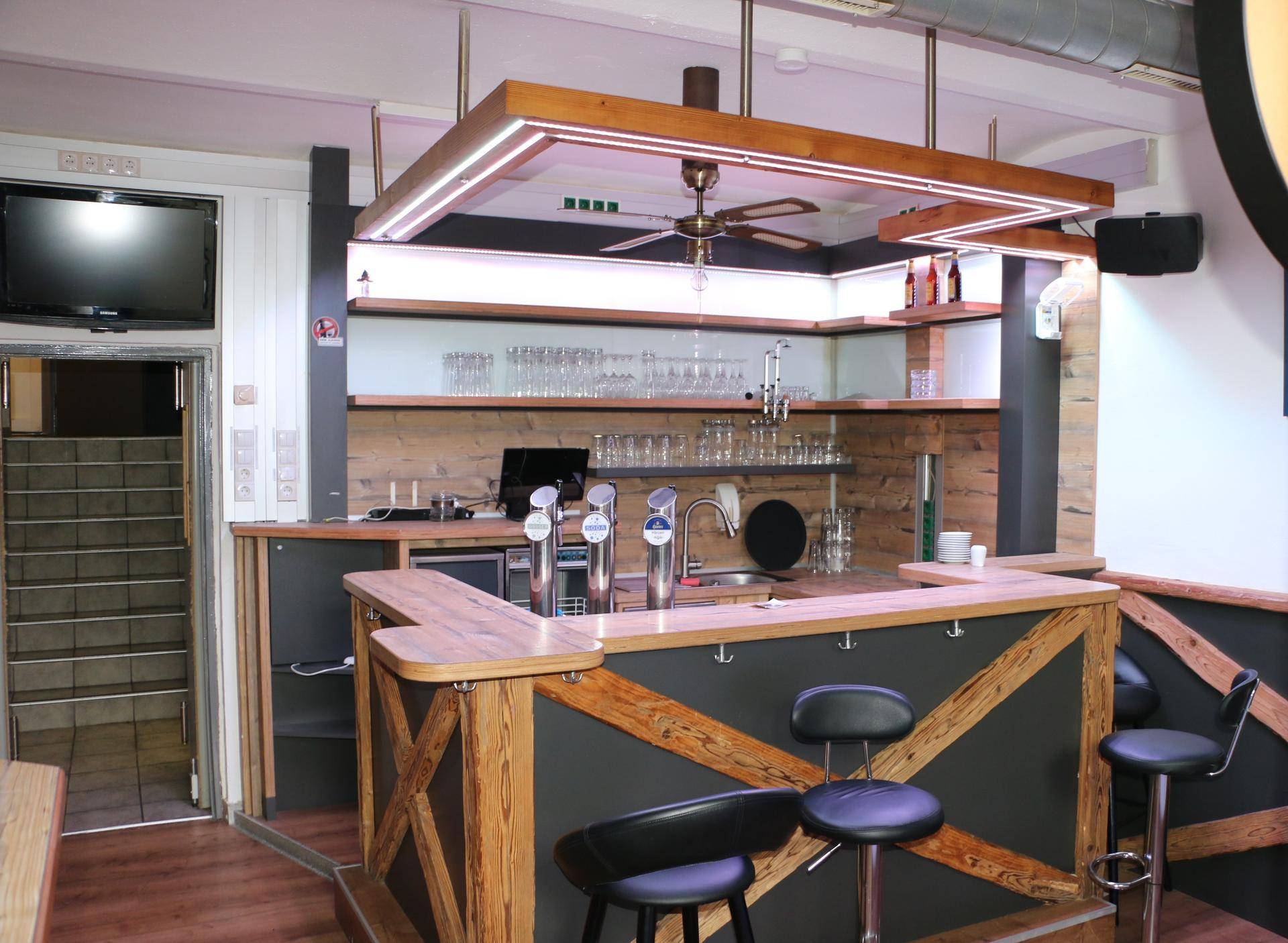 Gemütlicher Barbereich mit Holzelementen, Zapfanlage und Deckenventilator.