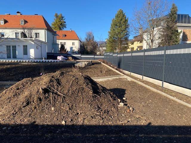 Gartenbereich in der Bauphase mit Erdhügeln und einem neuen Zaun im Hintergrund.