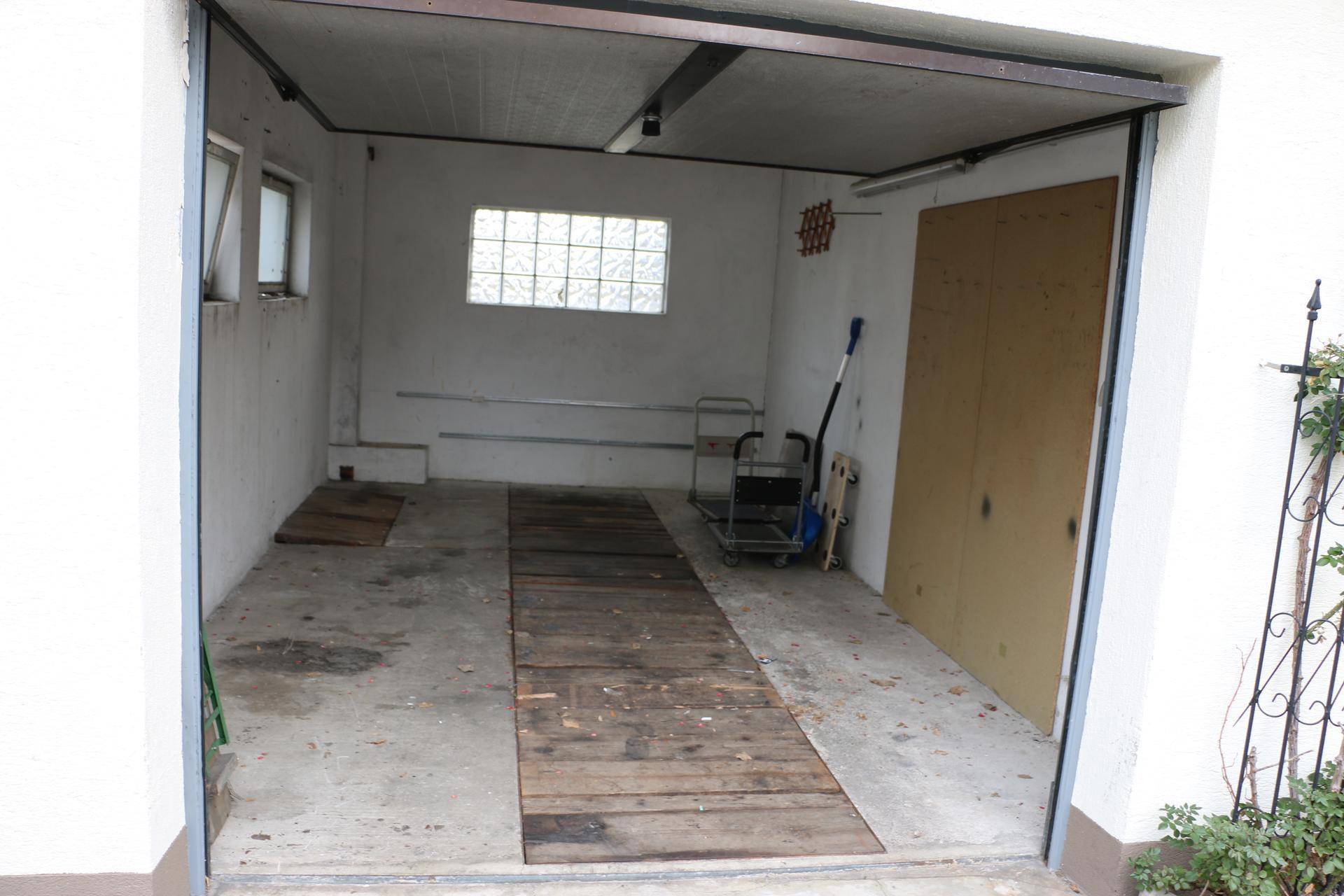 Einzelgarage mit Betonboden, Holzrampe und einem kleinen Fenster.