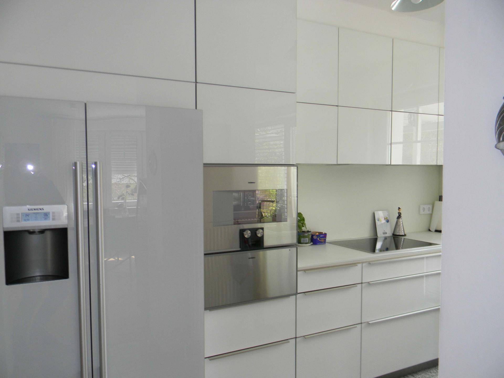 Moderne weiße Küche mit Hochglanzfronten, integrierten Siemens-Geräten und Kühlschrank.