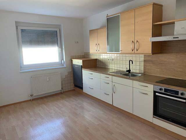 Funktionale Küche mit hellen Holzschränken, Fliesenrückwand und Fenster mit Rollladen.