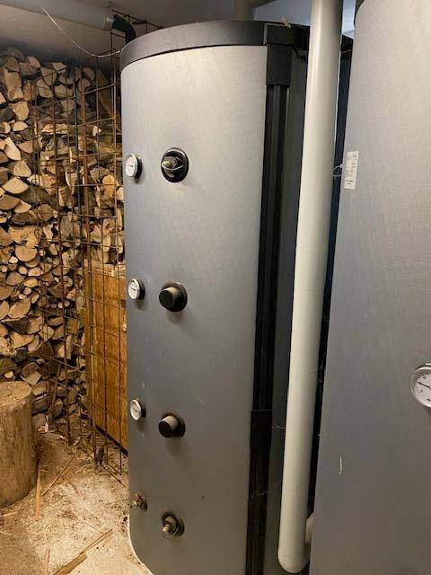 Technikraum mit großem Warmwasserspeicher und gestapeltem Brennholz für die Heizung.