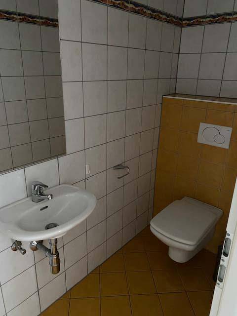 Gästetoilette mit gelben Bodenfliesen, weißen Wandfliesen und wandhängendem WC.