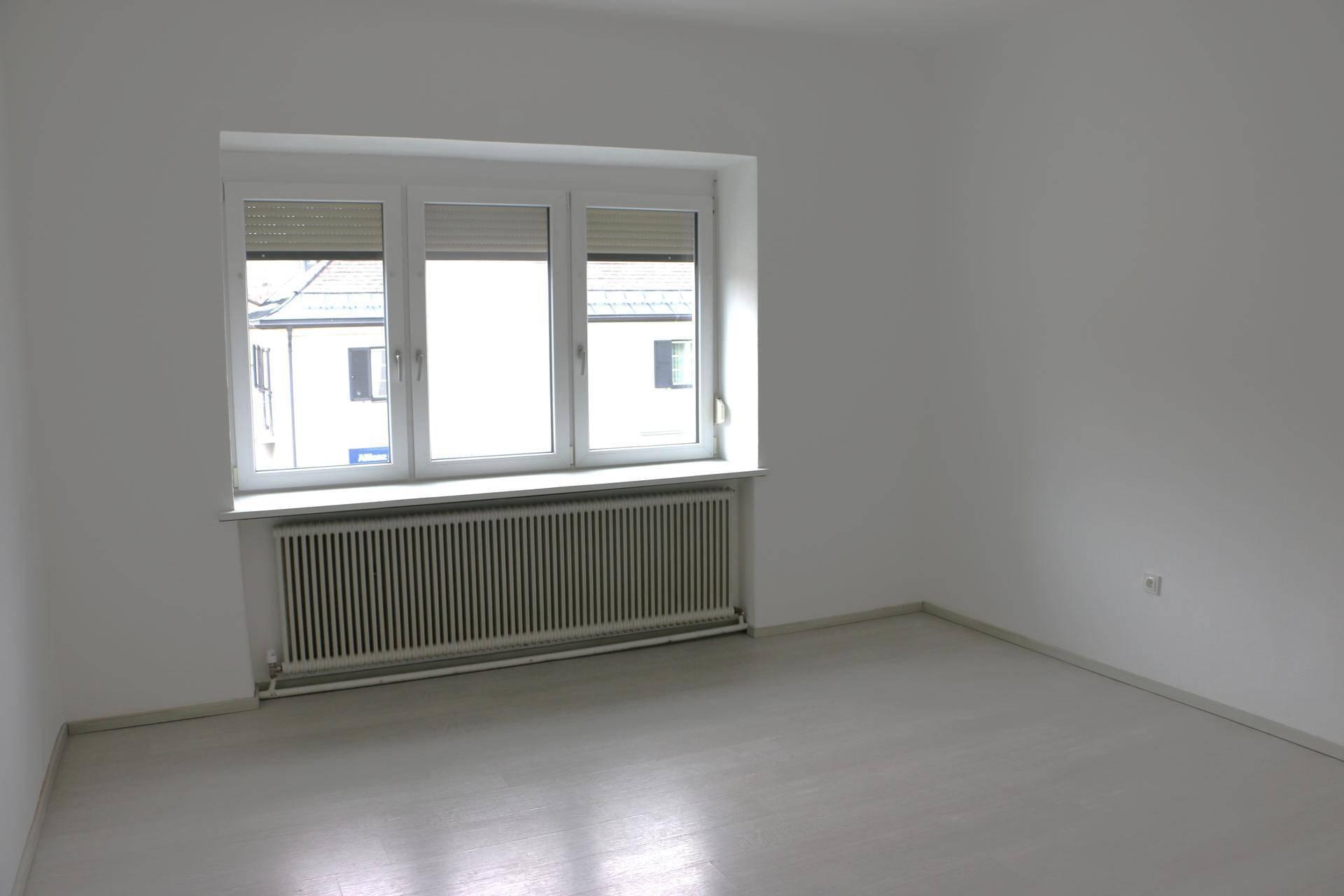 Unmöbliertes Zimmer mit hellem Boden, großem Fenster und Heizkörper unter der Fensterbank.