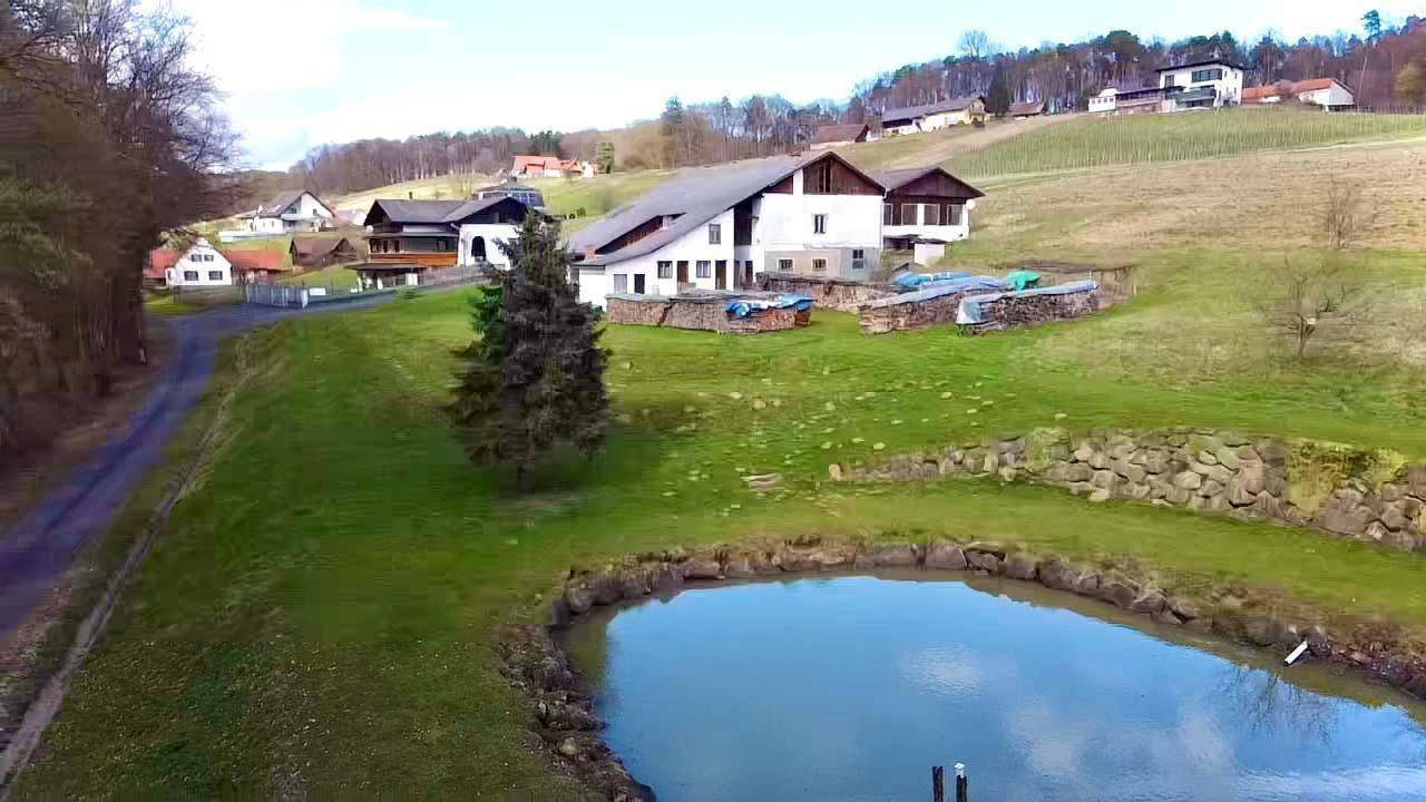 Panoramablick aus der Luft auf das Anwesen mit Teich, umgeben von grünen Hügeln und ländlicher Idylle.
