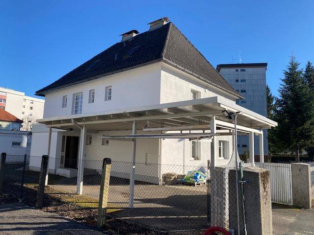 Haus mit großem Carport und Zaun, umgeben von anderen Gebäuden in der Nachbarschaft.