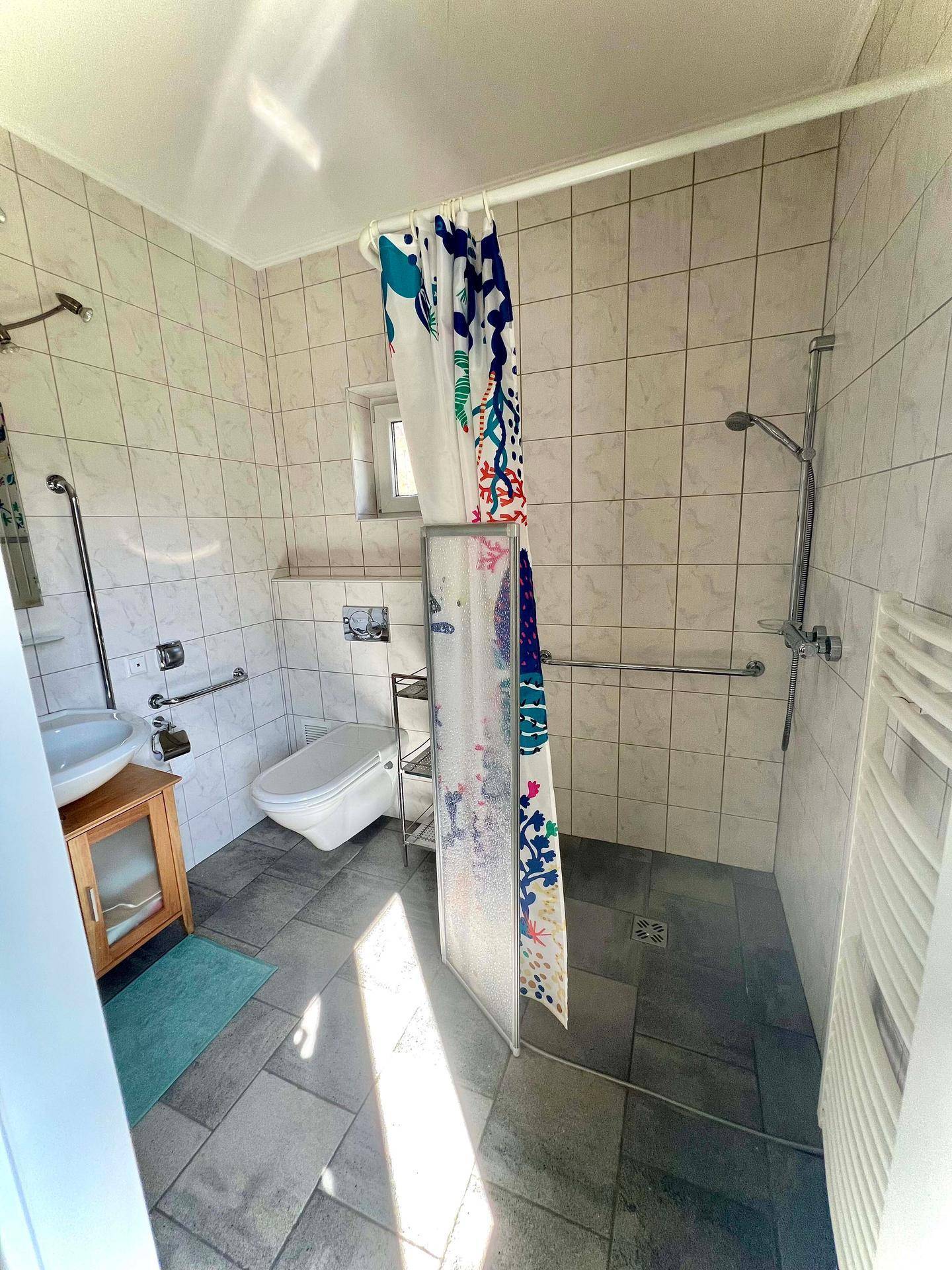 Helles Badezimmer mit barrierefreier Dusche, Haltegriffen und einem Fenster für Tageslicht.