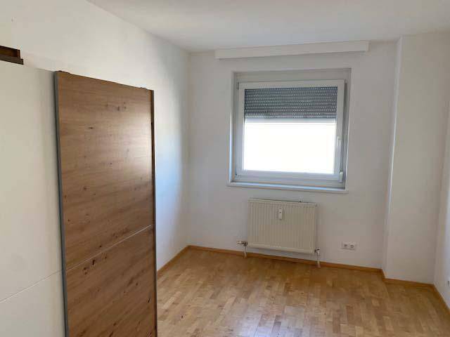 Helles Schlafzimmer mit Holzparkett, Heizkörper unter dem Fenster und Rollladen.