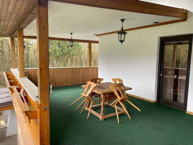 Überdachter Balkon mit Holztisch und Stühlen, ideal für Mahlzeiten im Freien mit Waldblick.